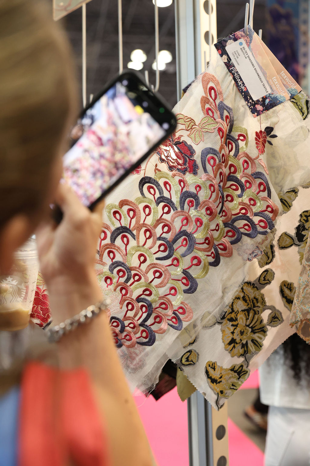 Attendee photographing intricately embroidered textile samples at Texworld Los Angeles