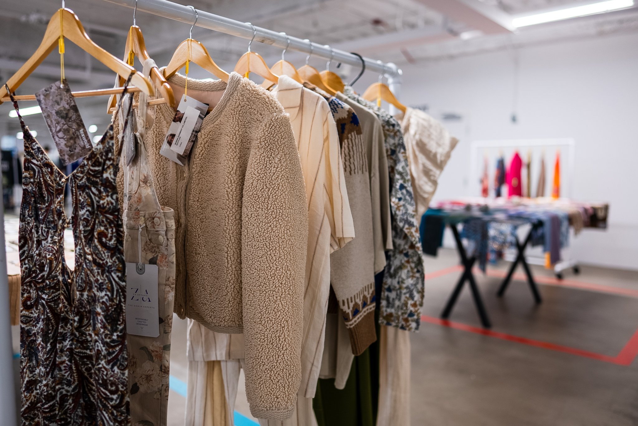 Rack displaying a variety of stylish clothing pieces, including a cozy beige fleece jacket, floral pants, and patterned tops, at a Texworld Los Angeles fashion exhibition.