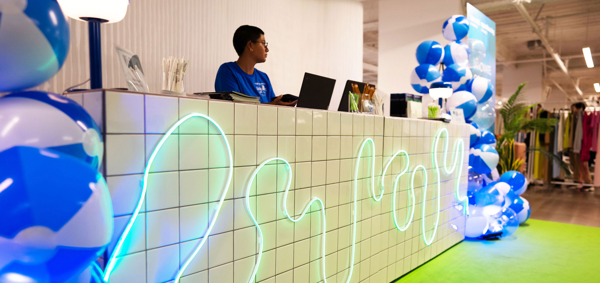Reception desk at Texworld Los Angeles with neon lights and blue-and-white balloons, featuring an event staff member working at a laptop